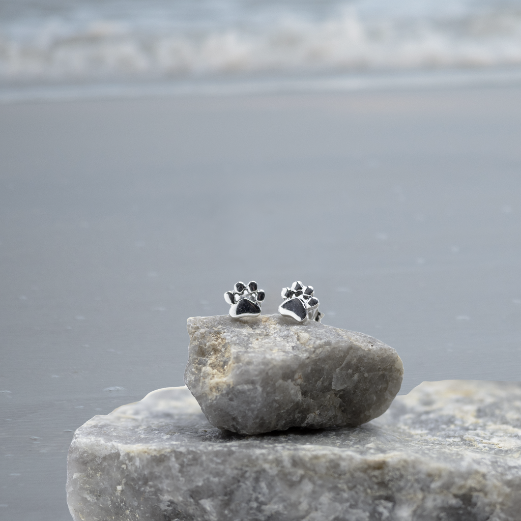 Pawsitively Perfect Paw Earrings balanced on a small rock. Sterling silver stud earrings.