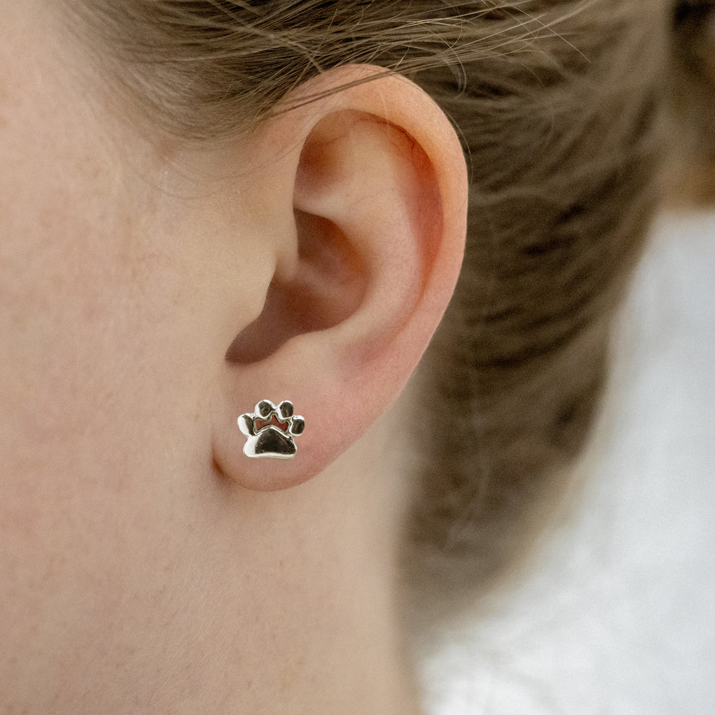 Sterling silver paw print earrings. Tiny studs on a model.