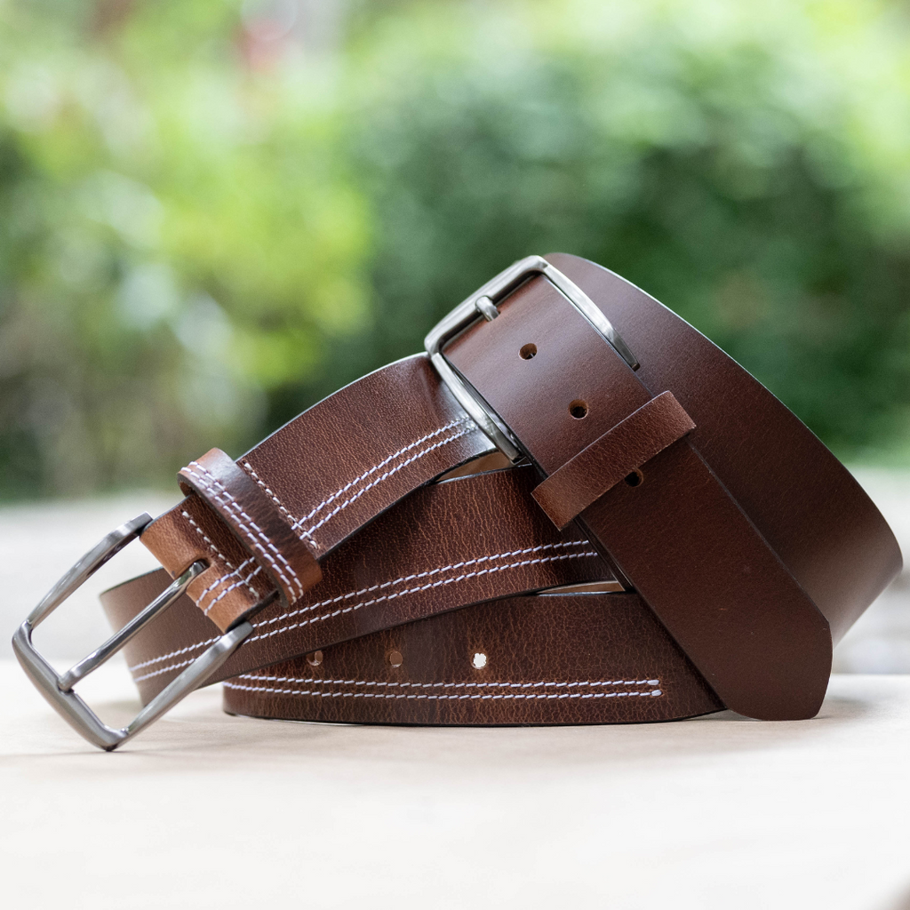 Millennial Brown and Brown Stitched Leather Belt Set. Outdoor setting. 1 solid brown, 1 with stitch.